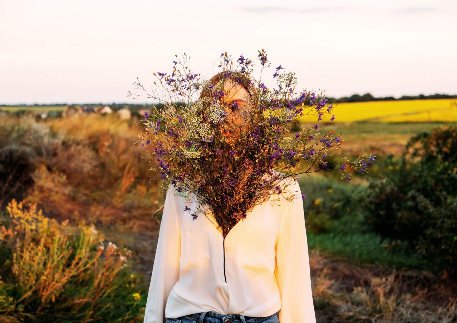 fiatal nő áll a mezőn virágokkal a mellkasán mentális egészséget képviselve