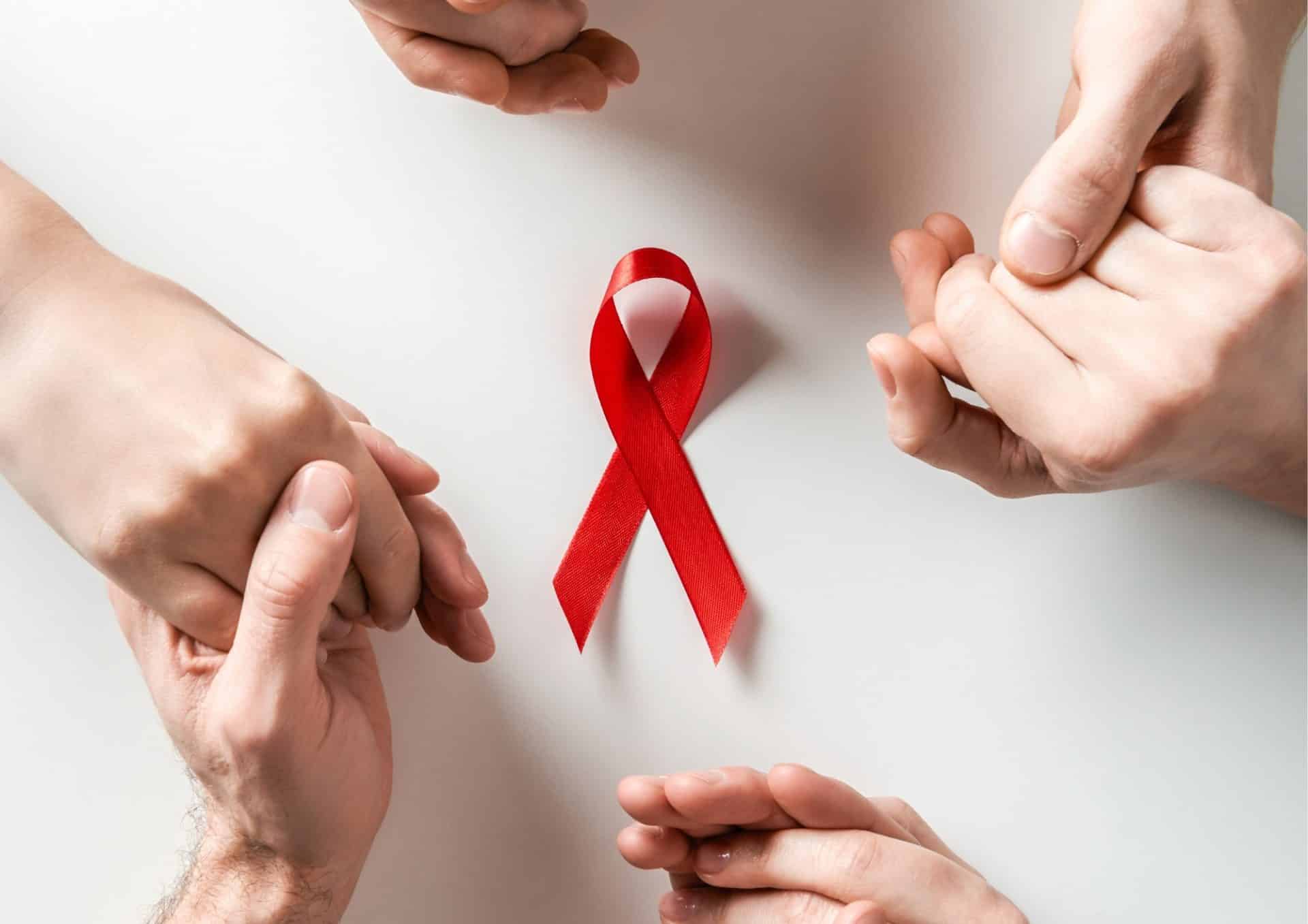 kézfejek egymásba fonódva piros szalaggal az AIDS összefogása ellen