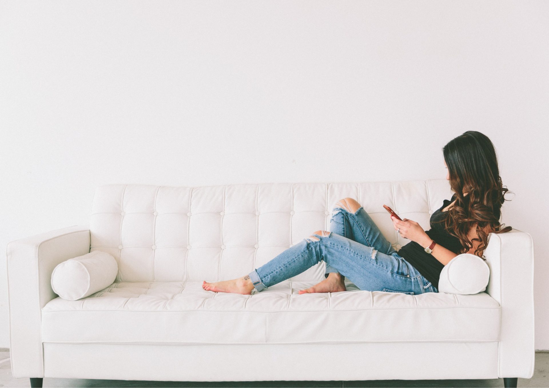 fiatal nő távkapcsolatban ül egyedül a kanapén a telefonját nézve