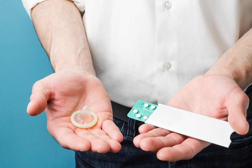 orvos fehér ingben a fogamzásgátlót és az óvszert mutatja be